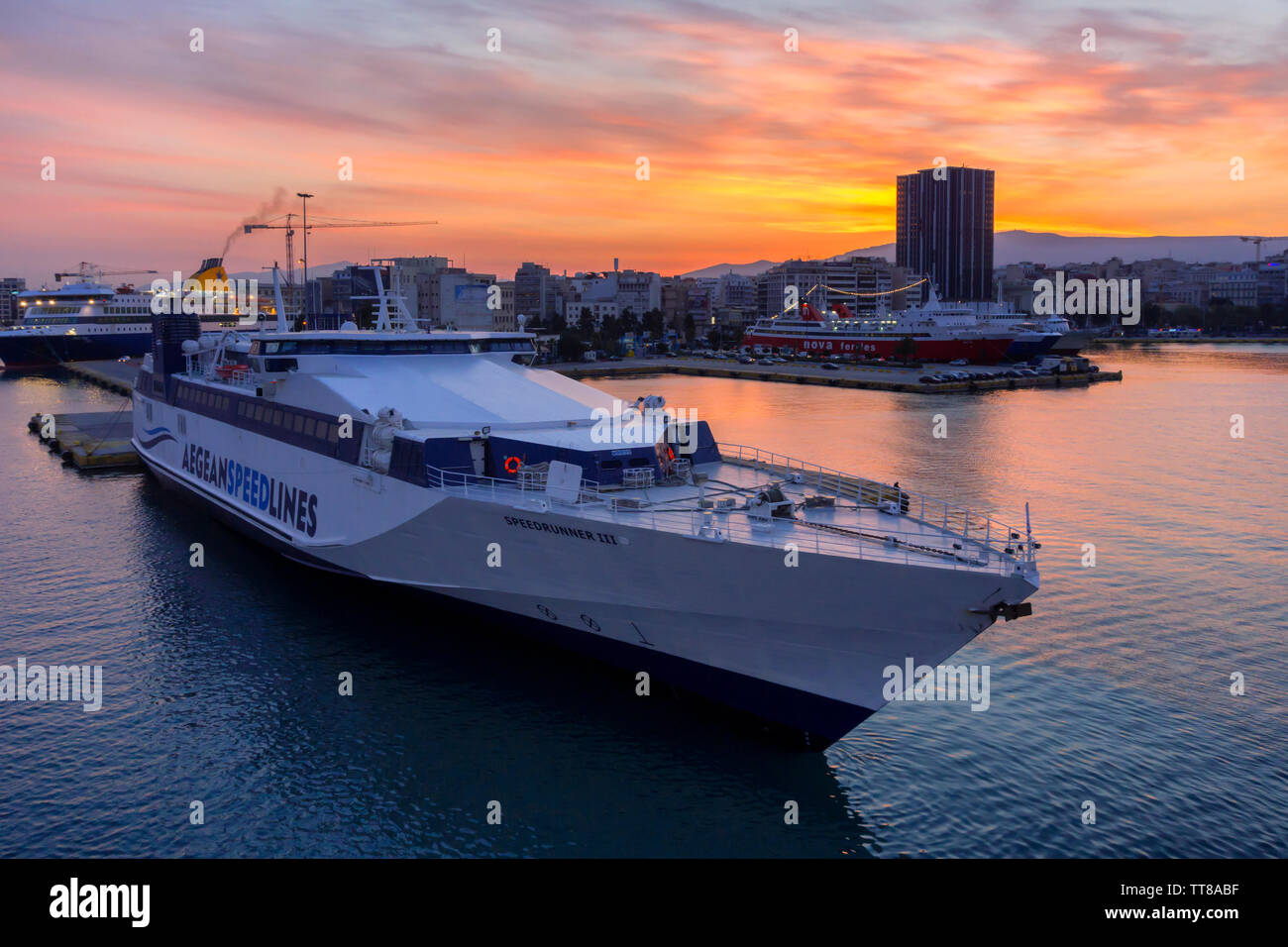 Il porto del Pireo, Attica / Grecia. Sunrise colorati con fiery il cielo sopra il porto e la città di Pireo. Le navi da passeggeri sono Ormeggiata al pontile Foto Stock