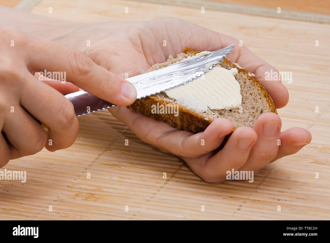 Donna mani diffusione di burro sul pezzo di pane di segale, primo piano Foto Stock