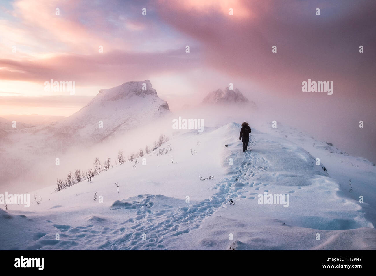 L'uomo alpinista camminando con footprint di neve sulla neve cresta Picco in blizzard al mattino Foto Stock