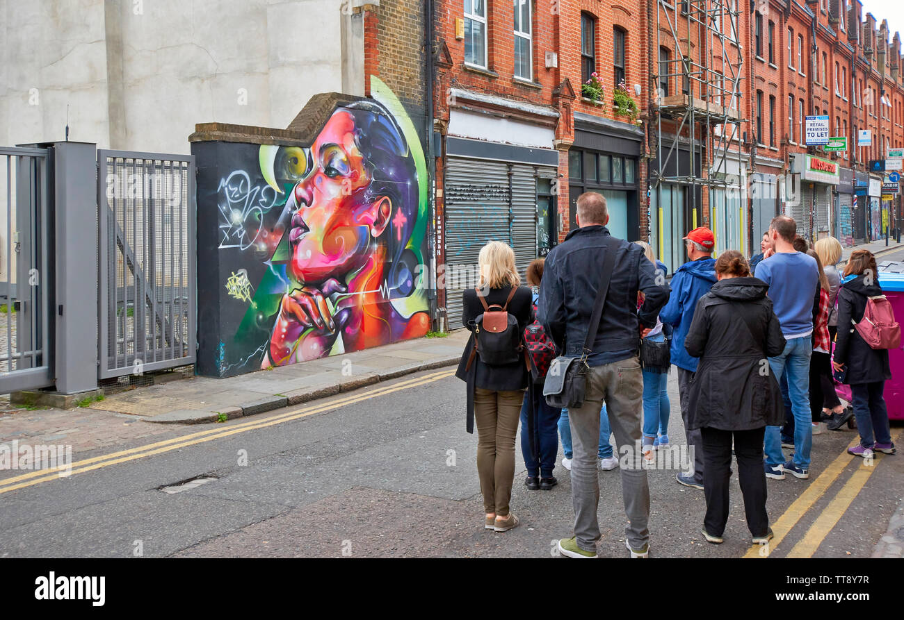 Londra Inghilterra Brick Lane gruppo di persone che studiano l'arte al muro nella zona Foto Stock