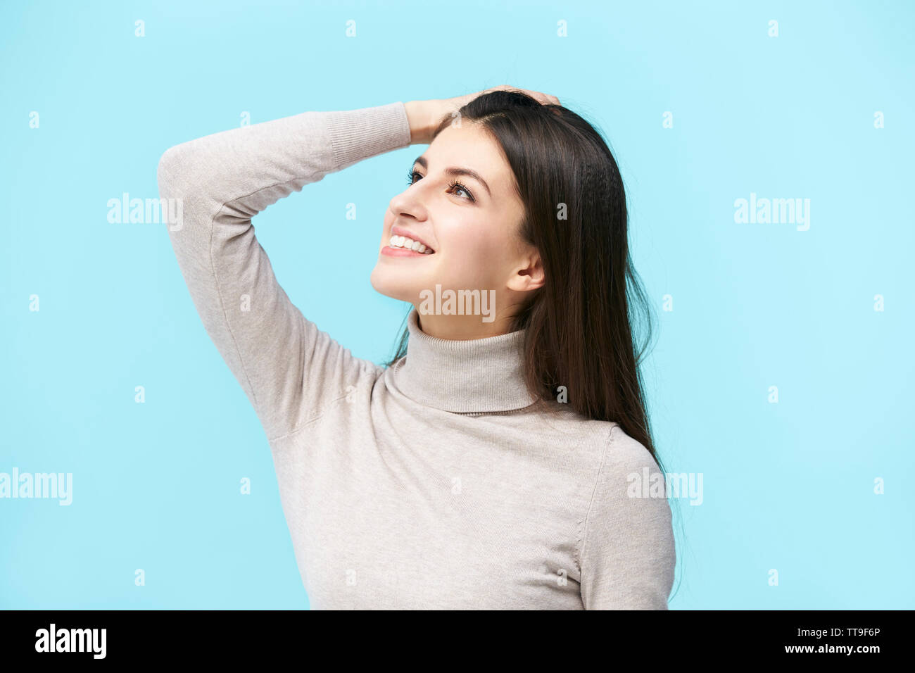 Bellissima giovane donna caucasica guardando verso l'alto e sorridente, mano sulla fronte, isolato su sfondo blu Foto Stock