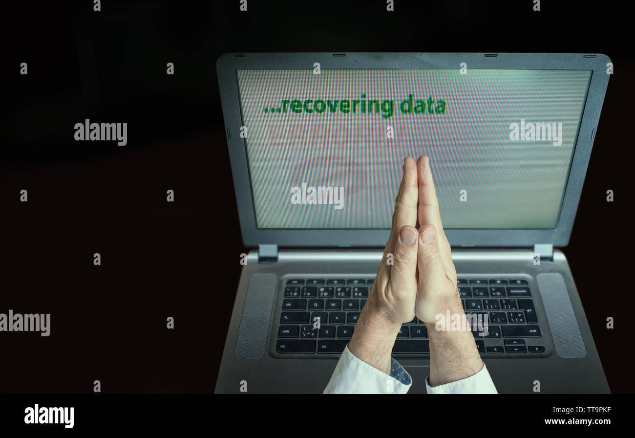 Due mani in una posizione di preghiera, grave angoscia, il computer ha problemi mi auguro è il recupero dei dati..low key, copy-spazio. Foto Stock