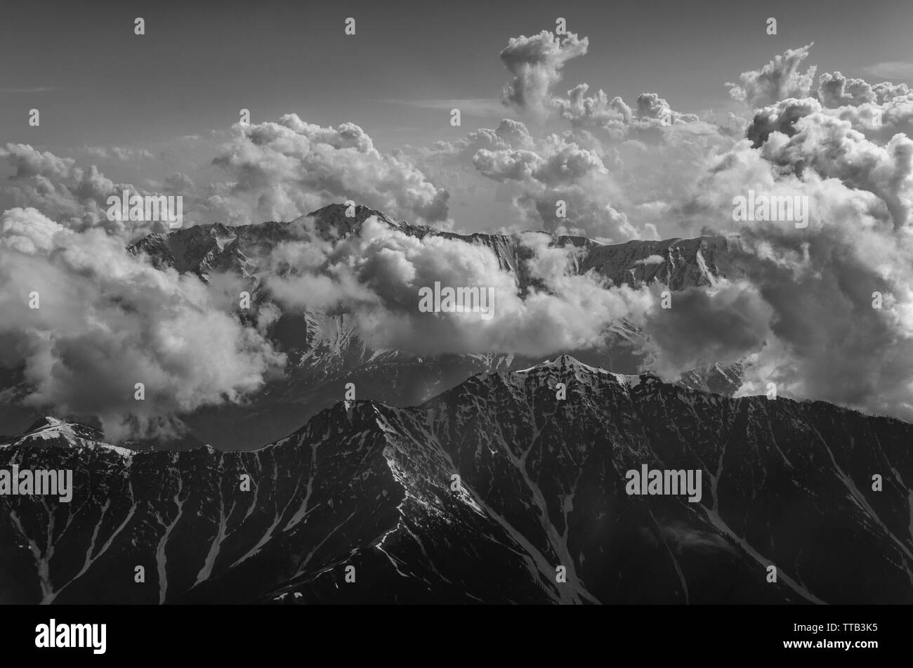 Fotografia in bianco e nero dell'ipnotizzante montagna himalayana peaking attraverso le nubi in un giorno nuvoloso di volo da Delhi a Srinagar. Foto Stock