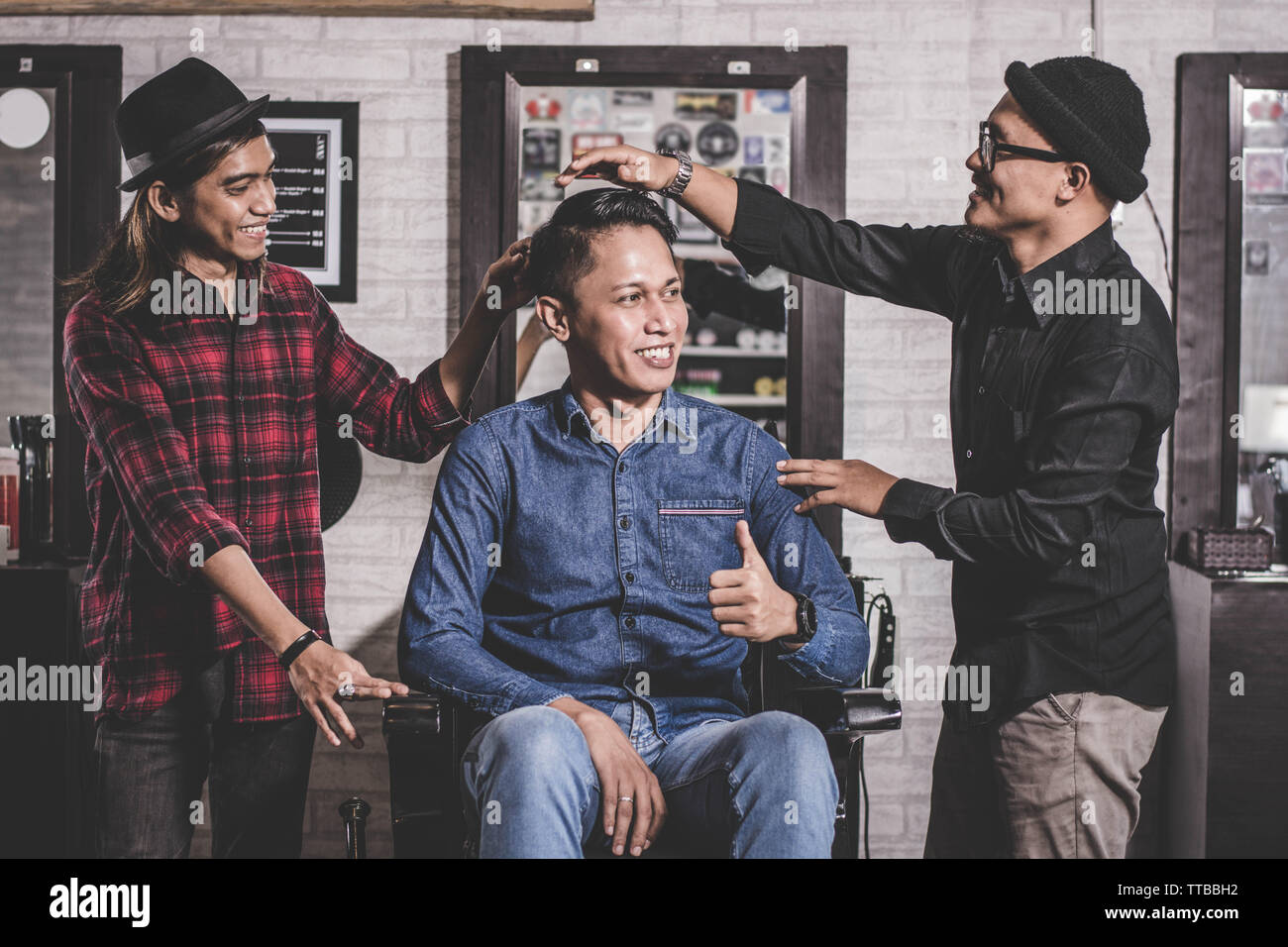 Ritratto di felice due barbiere con il cliente in piedi e sorridente a barberhop, hairstylisy e costumista il concetto di interazione Foto Stock