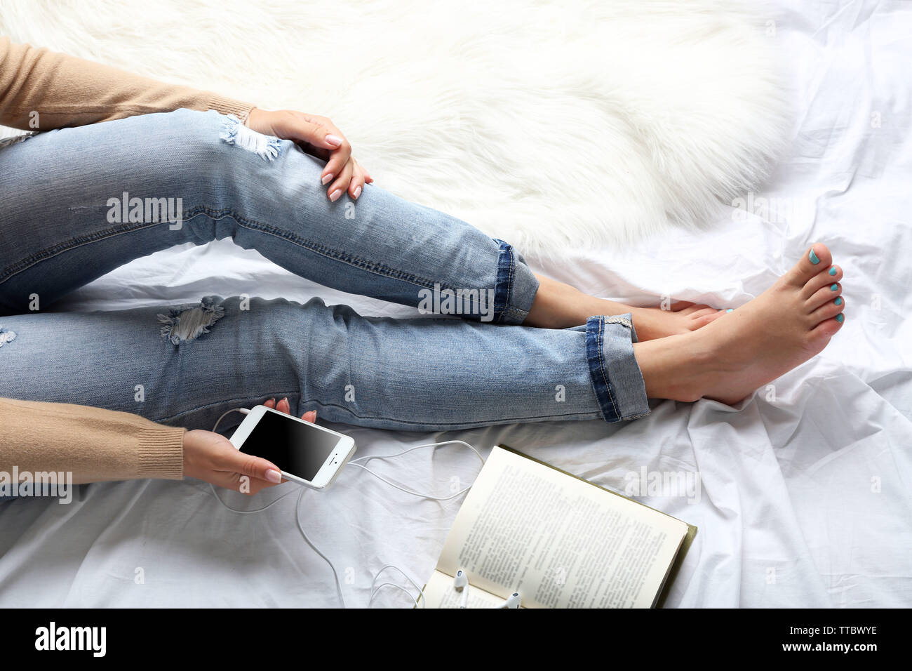 Donna in jeans blu guardando al telefono sul letto alto punto di vista Foto Stock