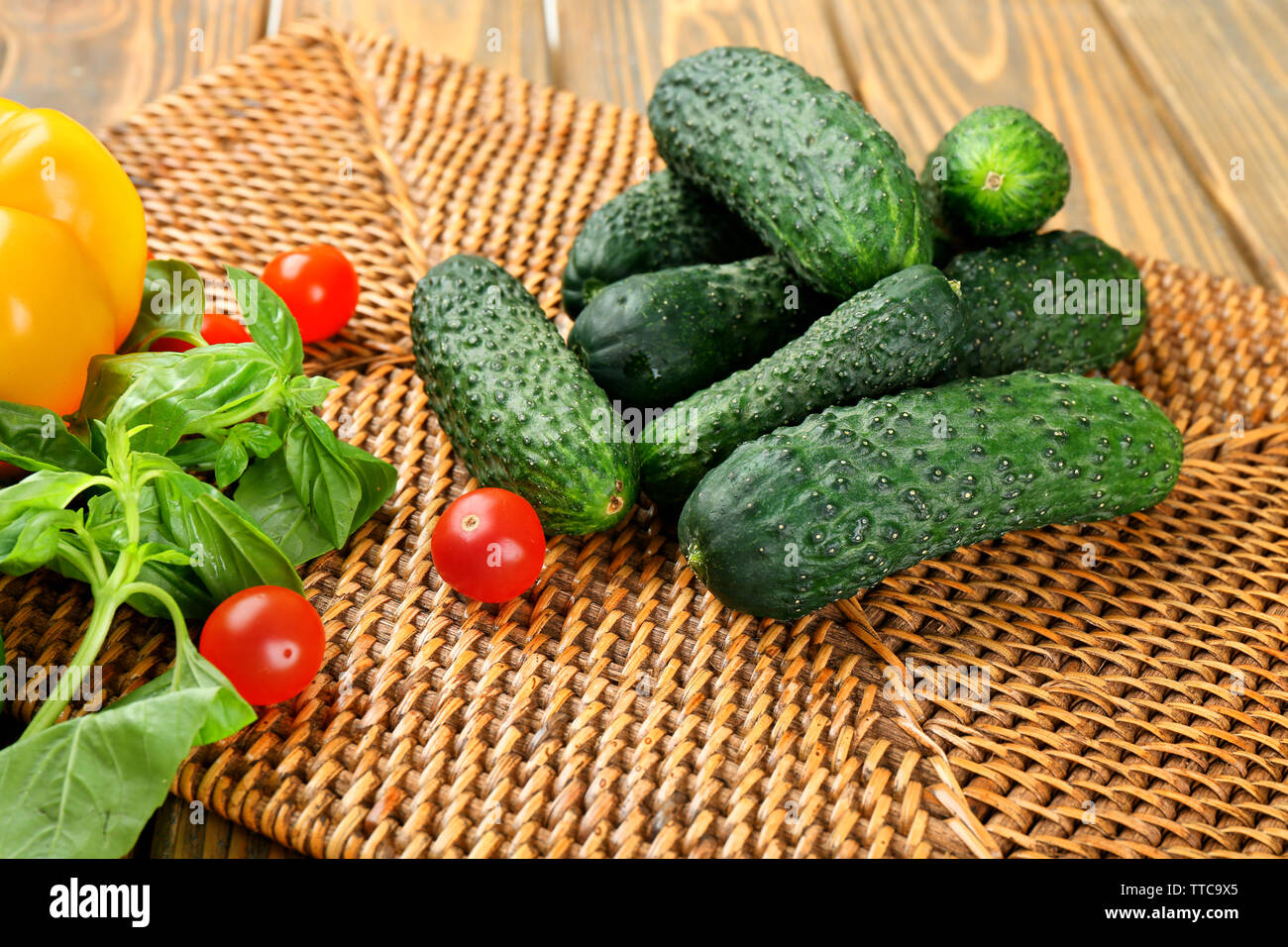 Composizione di cetrioli e pomodori e peperoni dolci sul tovagliolo di vimini contro lo sfondo di legno Foto Stock