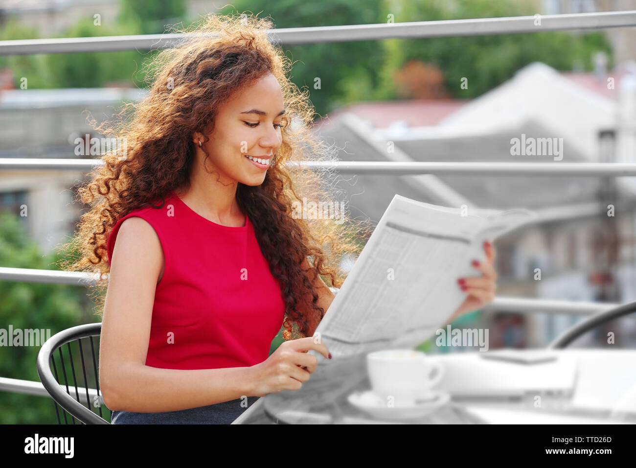 Ritratto di giovane donna graziosa in abito rosso lettura quotidiano a terrazza estiva Foto Stock