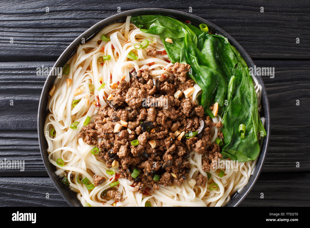 Cinese tradizionale Sichuan Dan Dan Tagliatelle con carne macinata e verdi in una piastra sul tavolo. Parte superiore orizzontale vista da sopra Foto Stock
