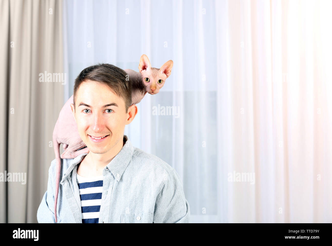 Giovane uomo bello tenendo un gatto sulla luce sullo sfondo di tulle Foto Stock