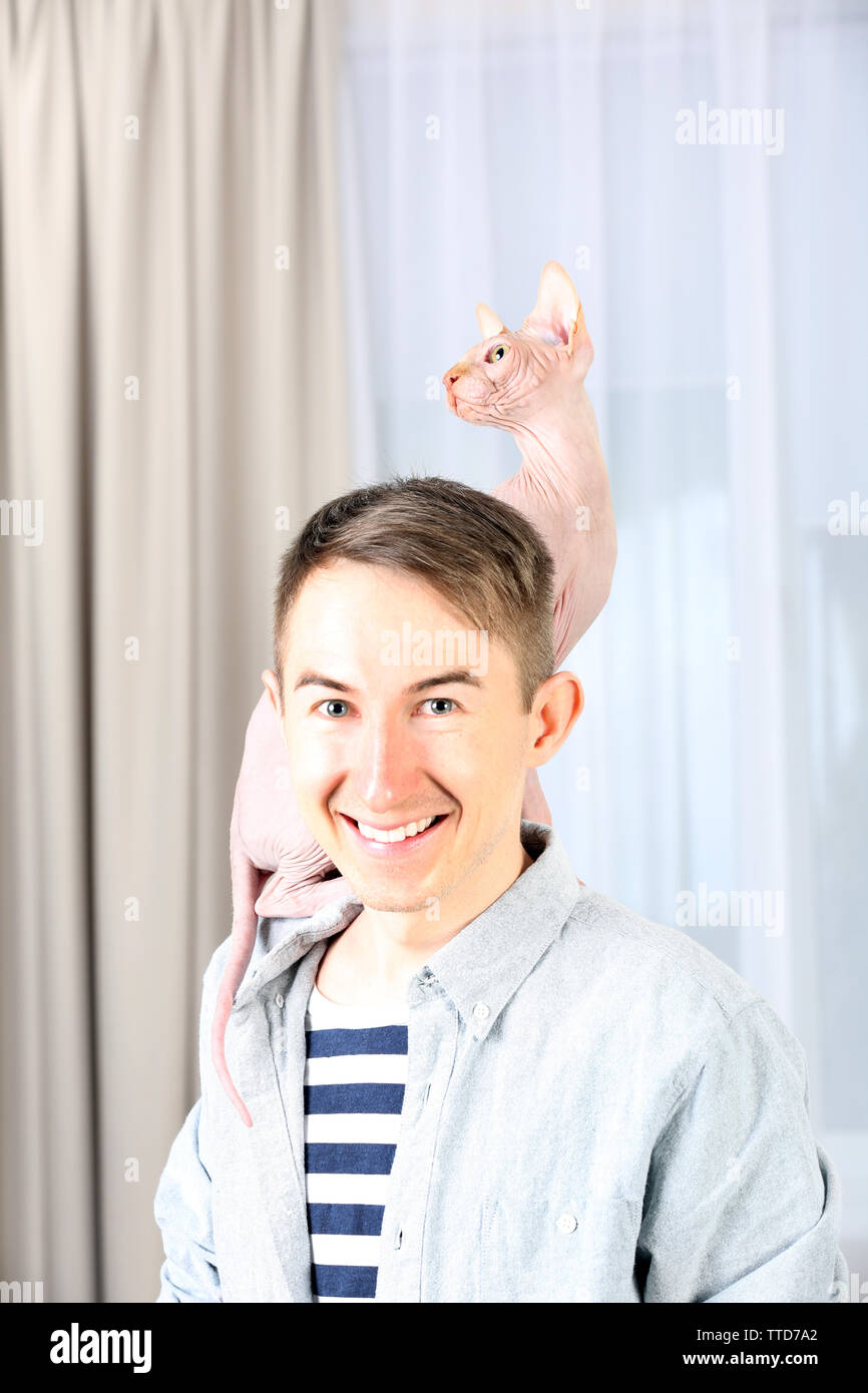 Giovane uomo bello tenendo un gatto sulla luce sullo sfondo di tulle Foto Stock