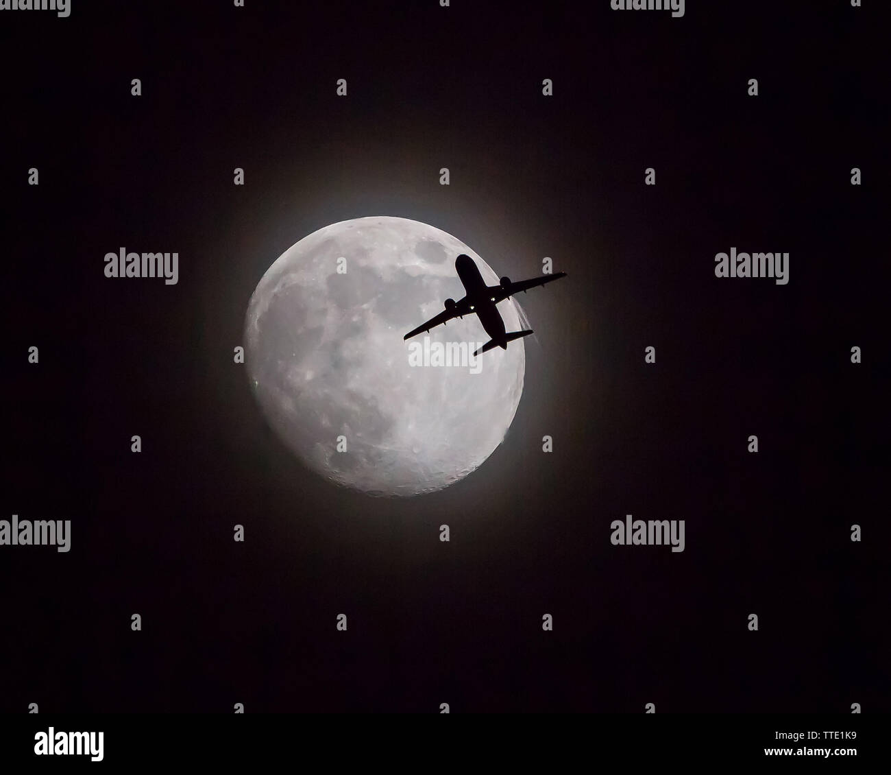 Un aereo commerciale attraversa nella parte anteriore di un near-luna piena poco dopo il decollo. Foto Stock
