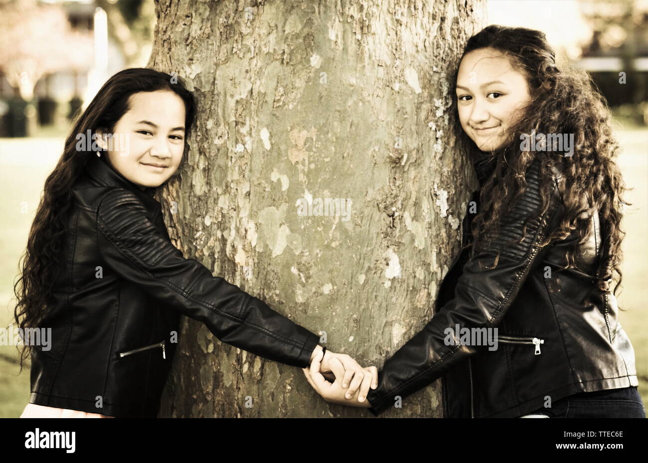 Due sorelle Maori holding hands abbracciando un albero all'aperto di giorno Foto Stock