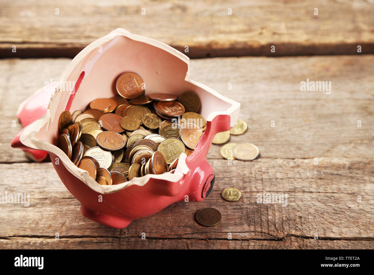 Rotto salvadanaio con monete su sfondo di legno Foto Stock