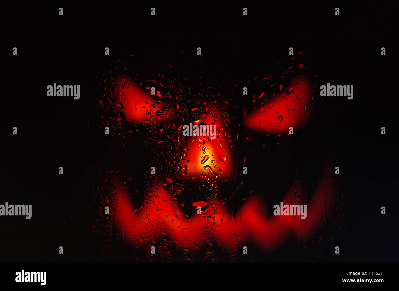 Scary faccia zucca attraverso il vetro bagnato con gocce dopo la pioggia Foto Stock