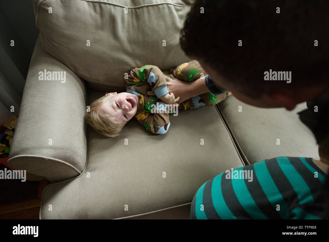 Papà solletica felice toddler figlio sul lettino mentre si gioca in casa Foto Stock