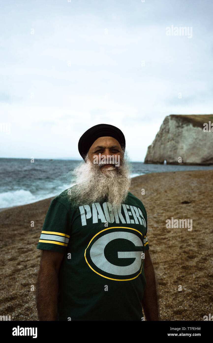 Un vecchio uomo in un turban sorge sulla spiaggia di Dorset Foto Stock