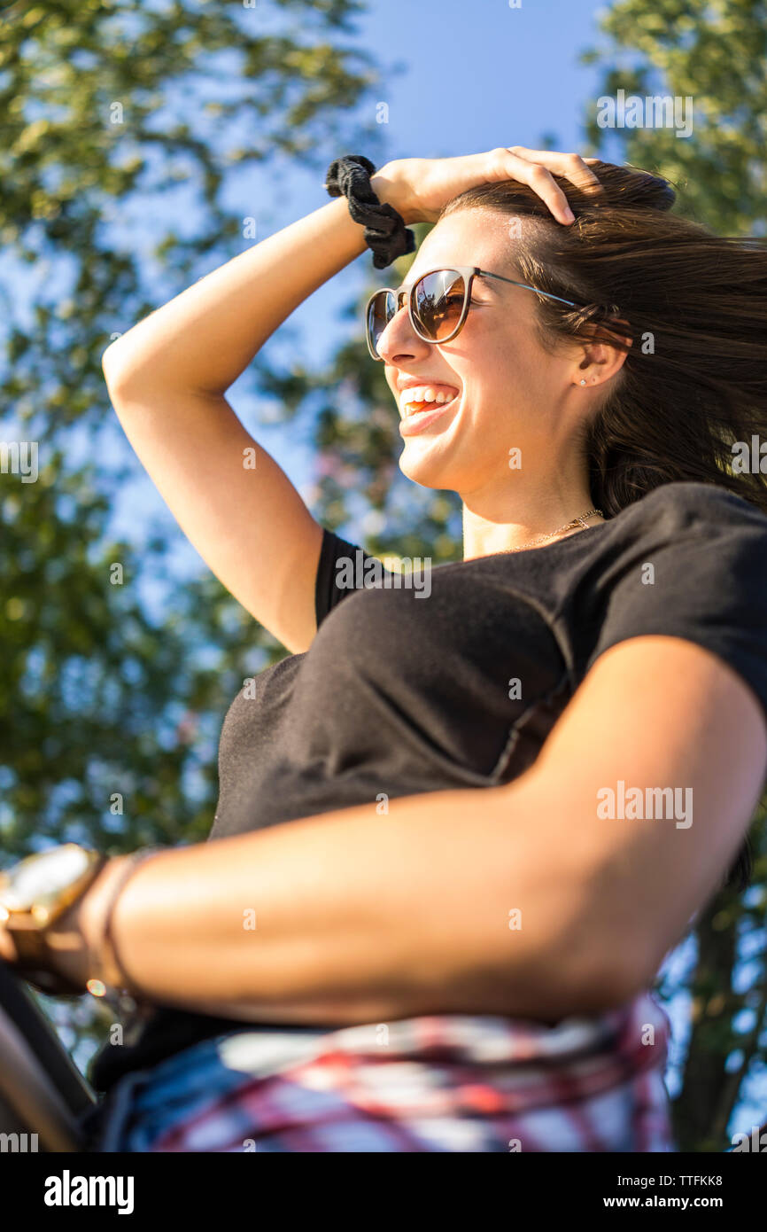 Giovani femmine tenendo i capelli indietro e sorridente felicemente durante l'estate Foto Stock