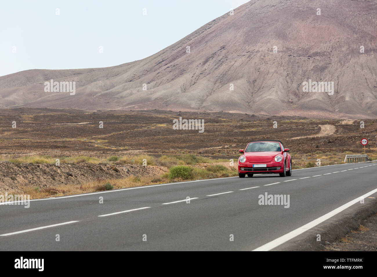 Red car guida nella vuota strada lastricata in un deserto paesaggio vulcanico Foto Stock