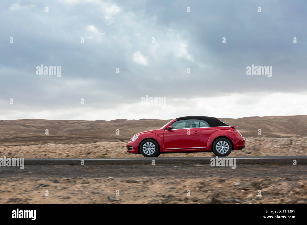 Red car guida nella vuota strada lastricata in un deserto paesaggio vulcanico Foto Stock