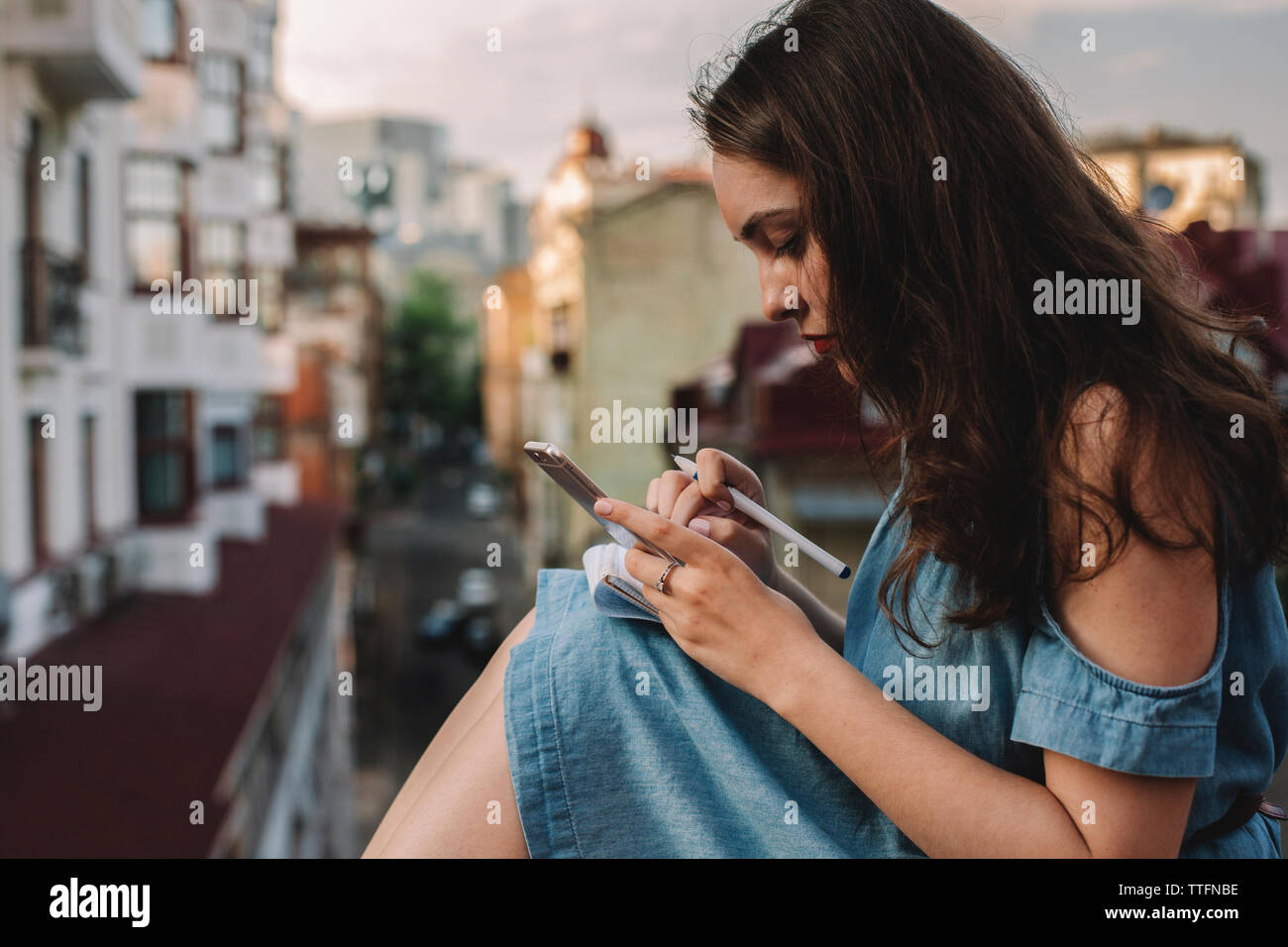 Vista laterale della giovane donna utilizzando smart phone seduti contro edifici in città Foto Stock