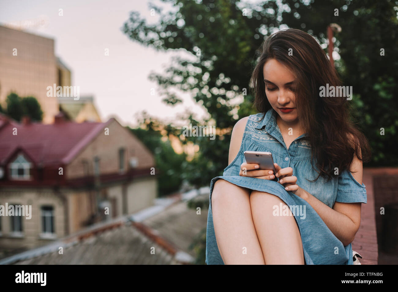 Giovane donna utilizzando smart phone mentre è seduto sulla parete di ritegno in città Foto Stock