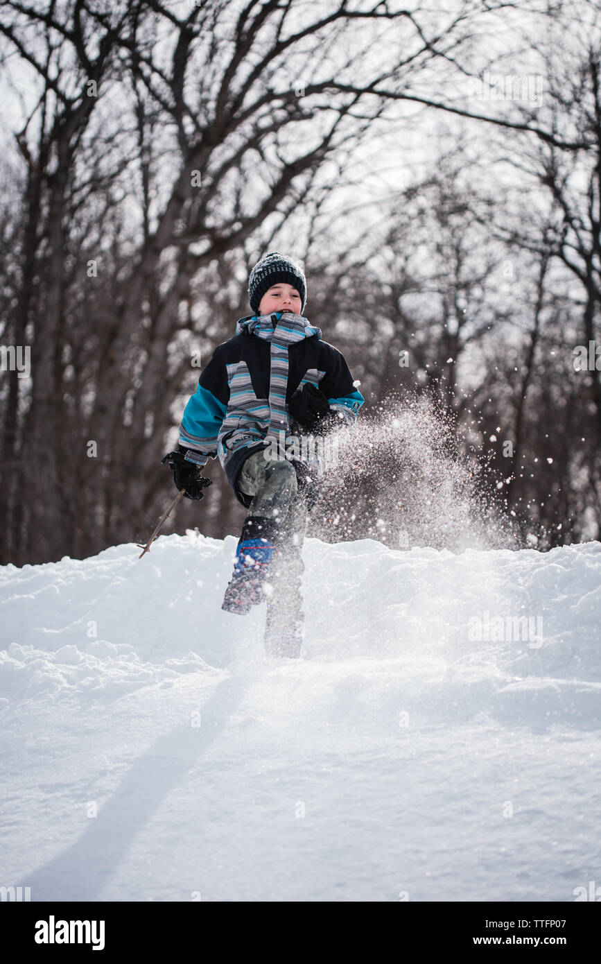 Ragazzo giovane calci neve in aria su una giornata invernale nella zona boschiva. Foto Stock