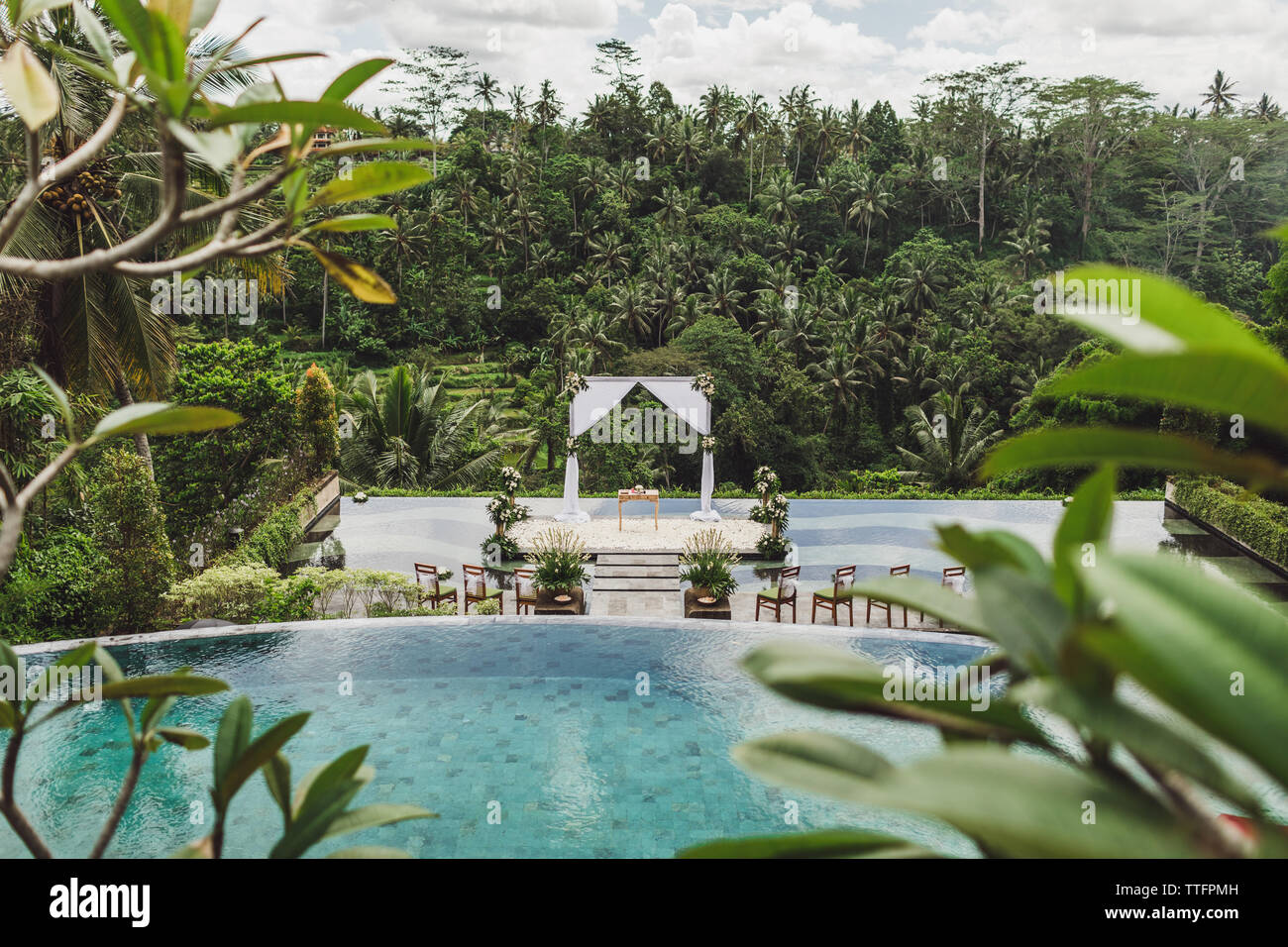 Bianco cerimonia di nozze arch nella giungla tropicale sul bordo del blu piscina infinity. Bellissimo arco e decori sulla scogliera. Vista da sopra. Foto Stock