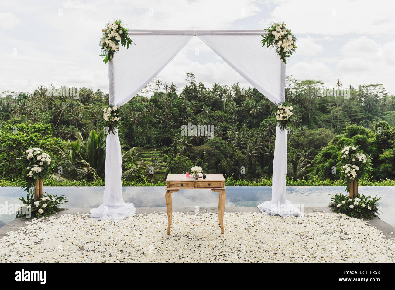 Bianco cerimonia di nozze arch nella giungla tropicale sul bordo del blu piscina infinity. Bellissimo arco e decori sulla scogliera. Foto Stock