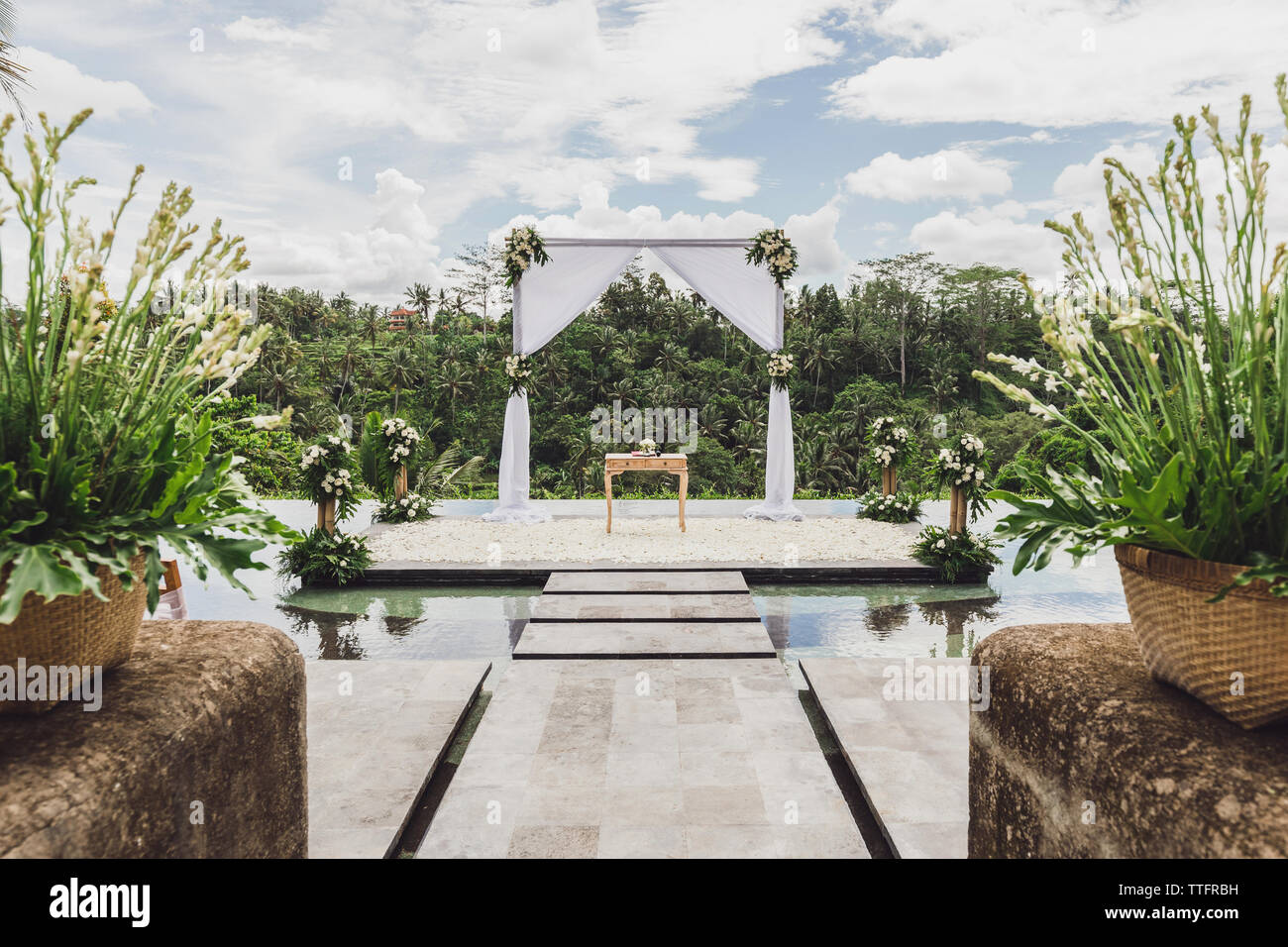 Bianco cerimonia di nozze arch nella giungla tropicale sul bordo del blu piscina infinity. Bellissimo arco e decori sulla scogliera. Foto Stock