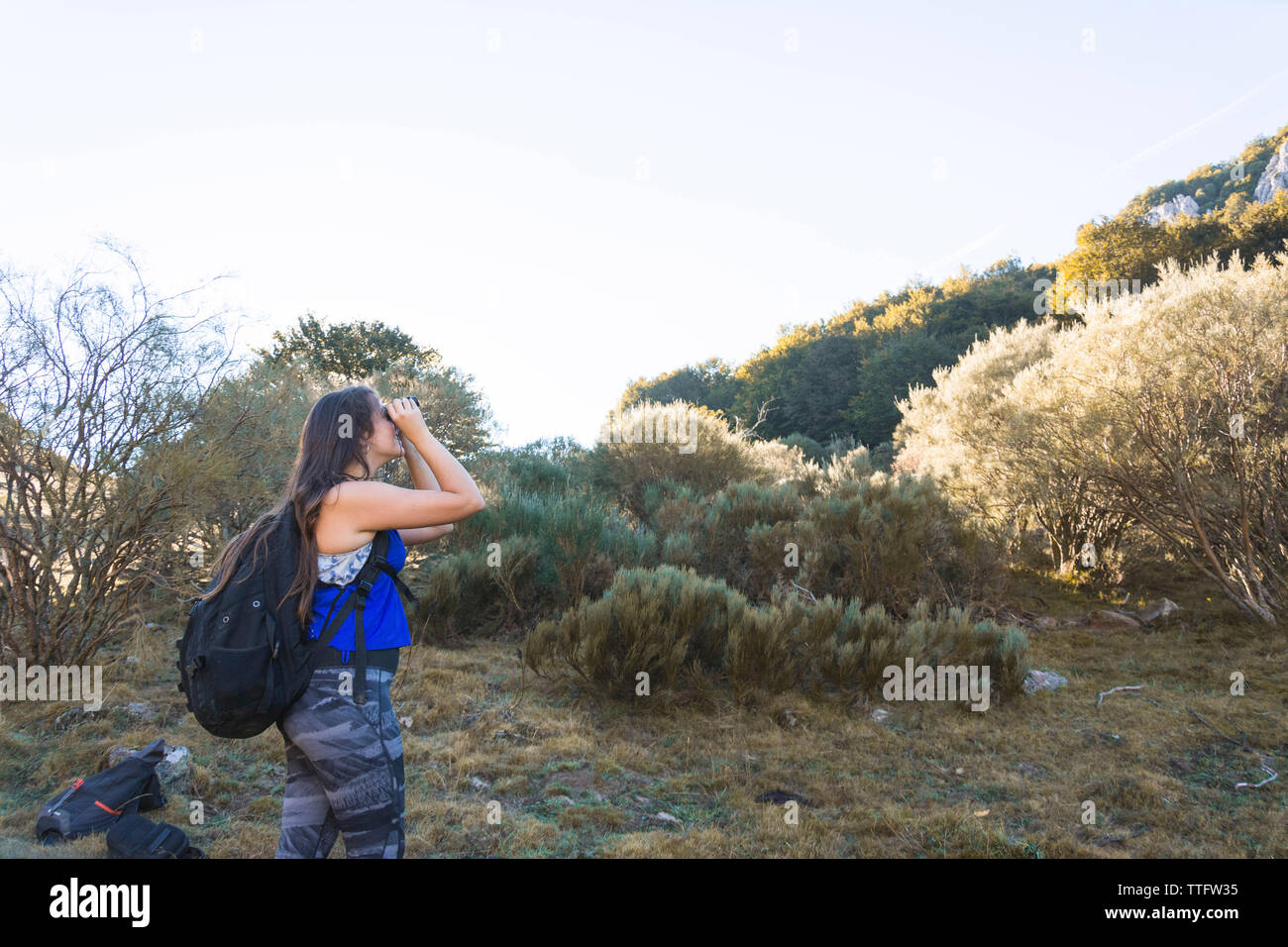 Vista laterale di un escursionista femmina con zaino guardando attraverso il binocolo mentre si sta in piedi sul campo contro sky Foto Stock