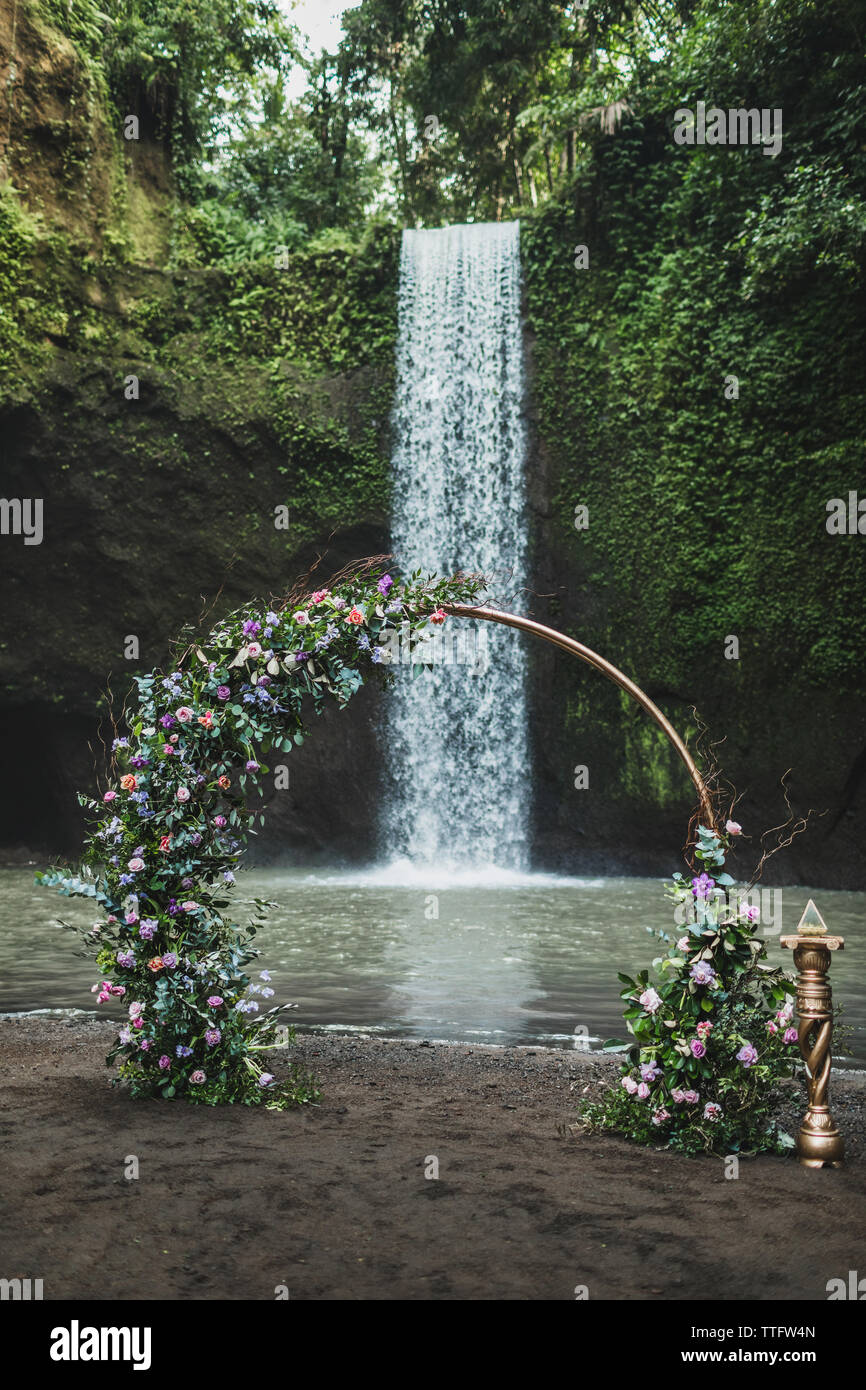 Rotondo di metallo arco di nozze decorata con viola e verde fiori sulla cascata Tibumana, Bali. Stile moderno, matrimonio e il concetto di amore. Foto Stock