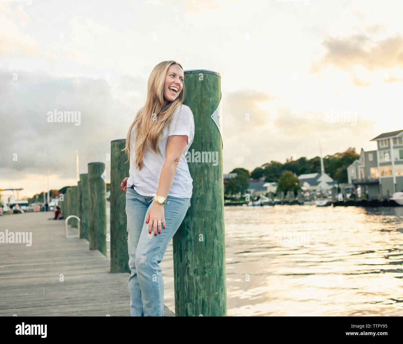 Donna felice urlando mentre si sta in piedi sul molo sul fiume contro il cielo durante il tramonto Foto Stock