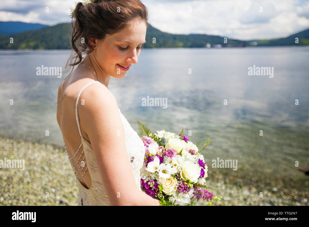 Vista laterale della sposa sorridente con bouquet in piedi sul lungolago Foto Stock