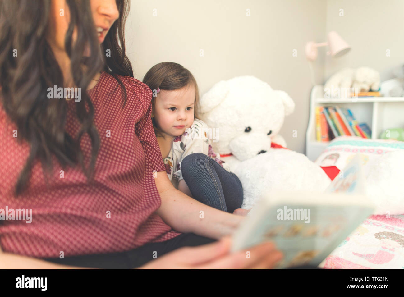 Madre libro lettura mentre è seduto con la figlia sul letto di casa Foto Stock