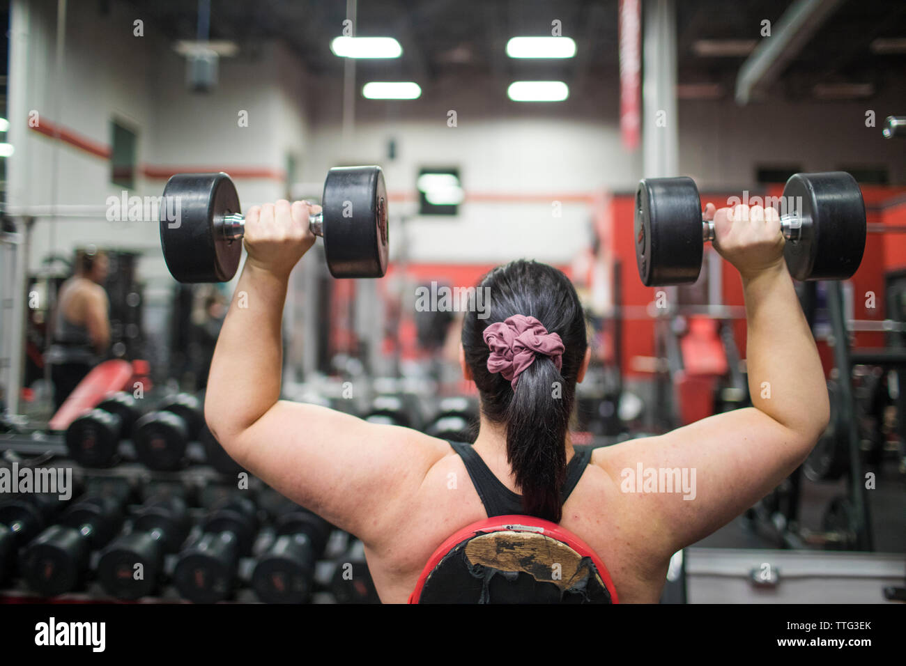 Vista posteriore della donna forte esercizio con manubri in palestra. Foto Stock