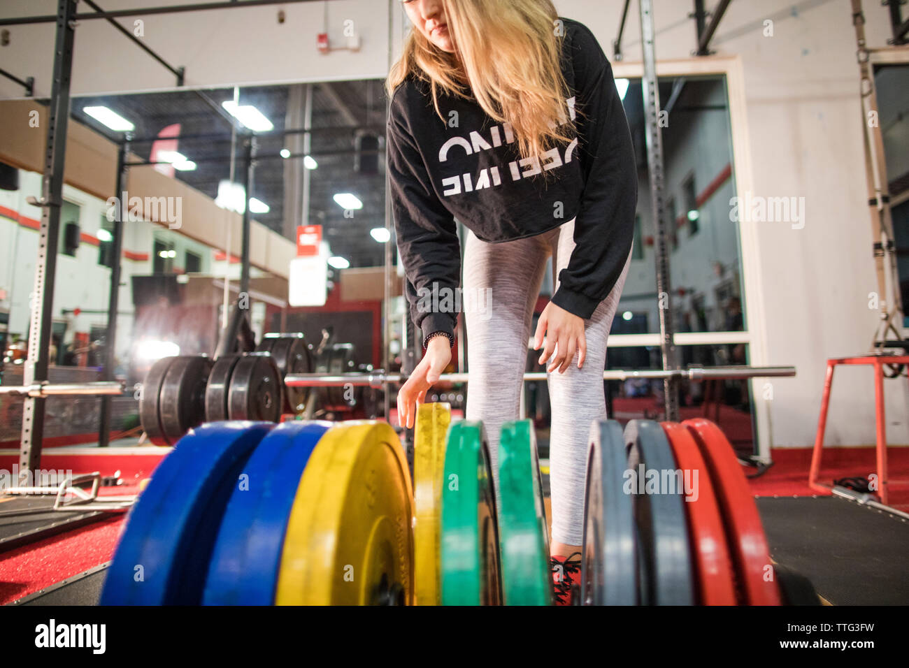 Giovane donna seleziona barbell pesi dal rack peso in palestra Foto Stock