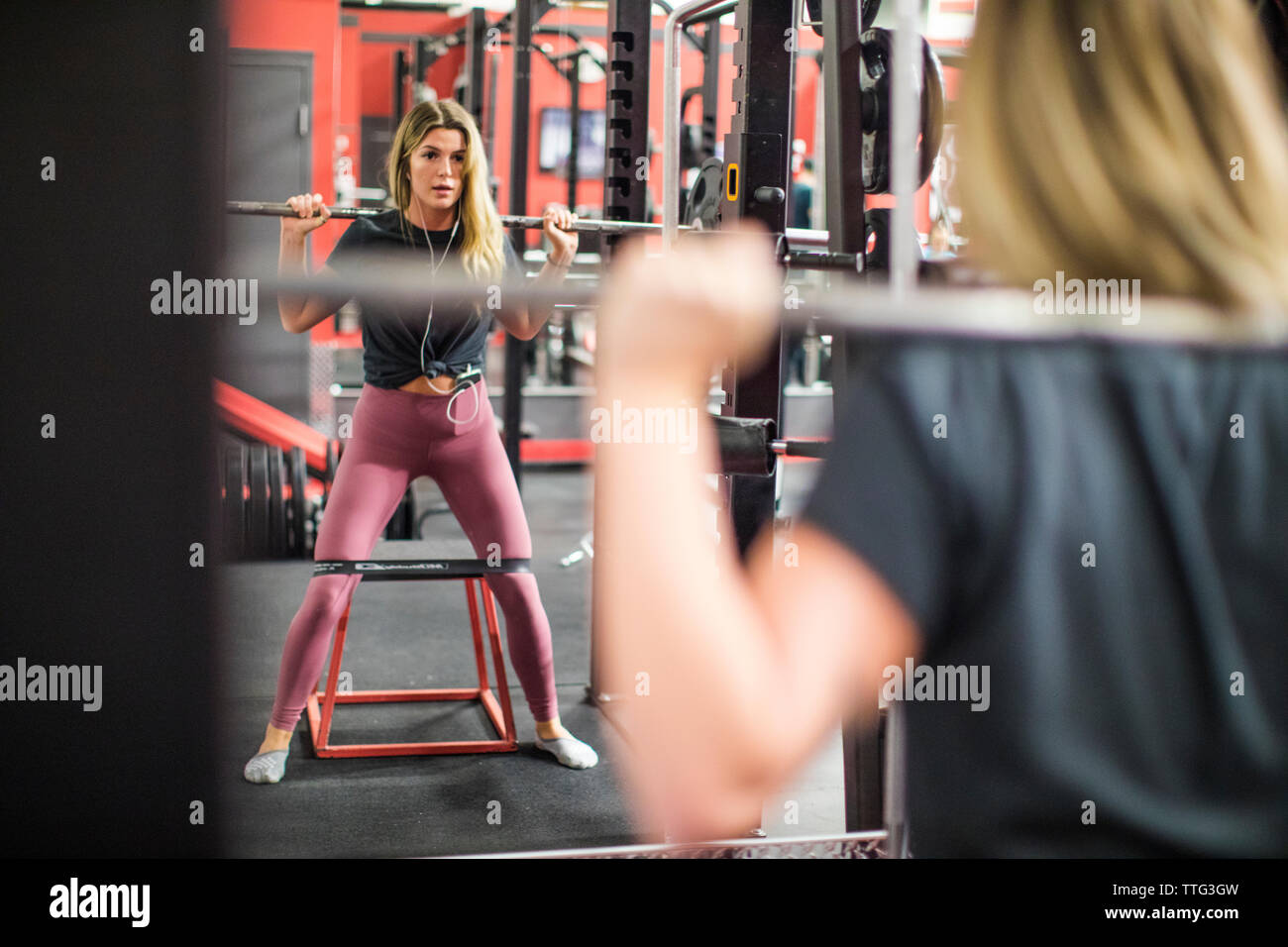 La riflessione di donna attraente la formazione su squat rack in palestra. Foto Stock