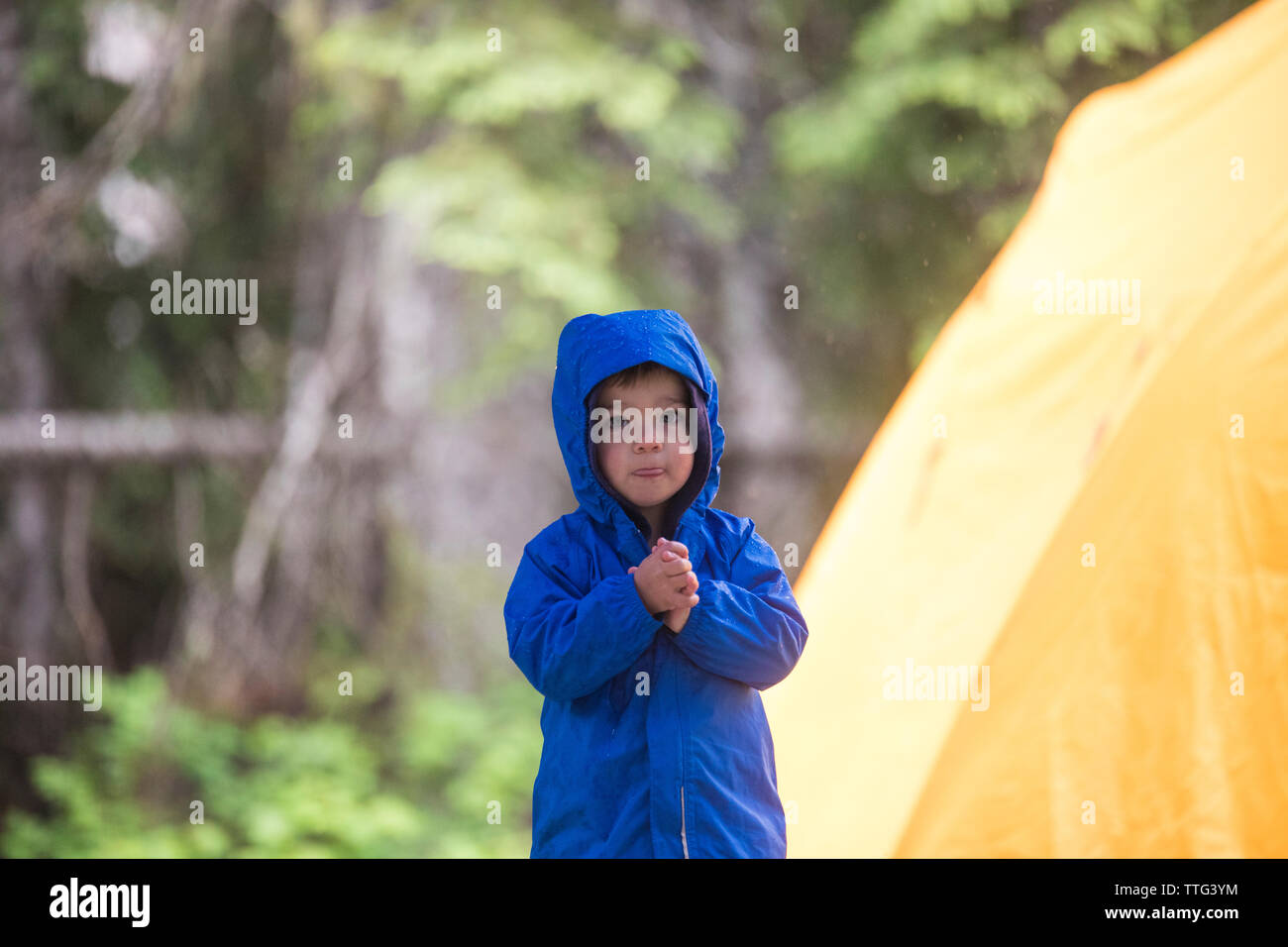 Il freddo toddler sorge accanto alla tenda durante una tempesta di pioggia Foto Stock