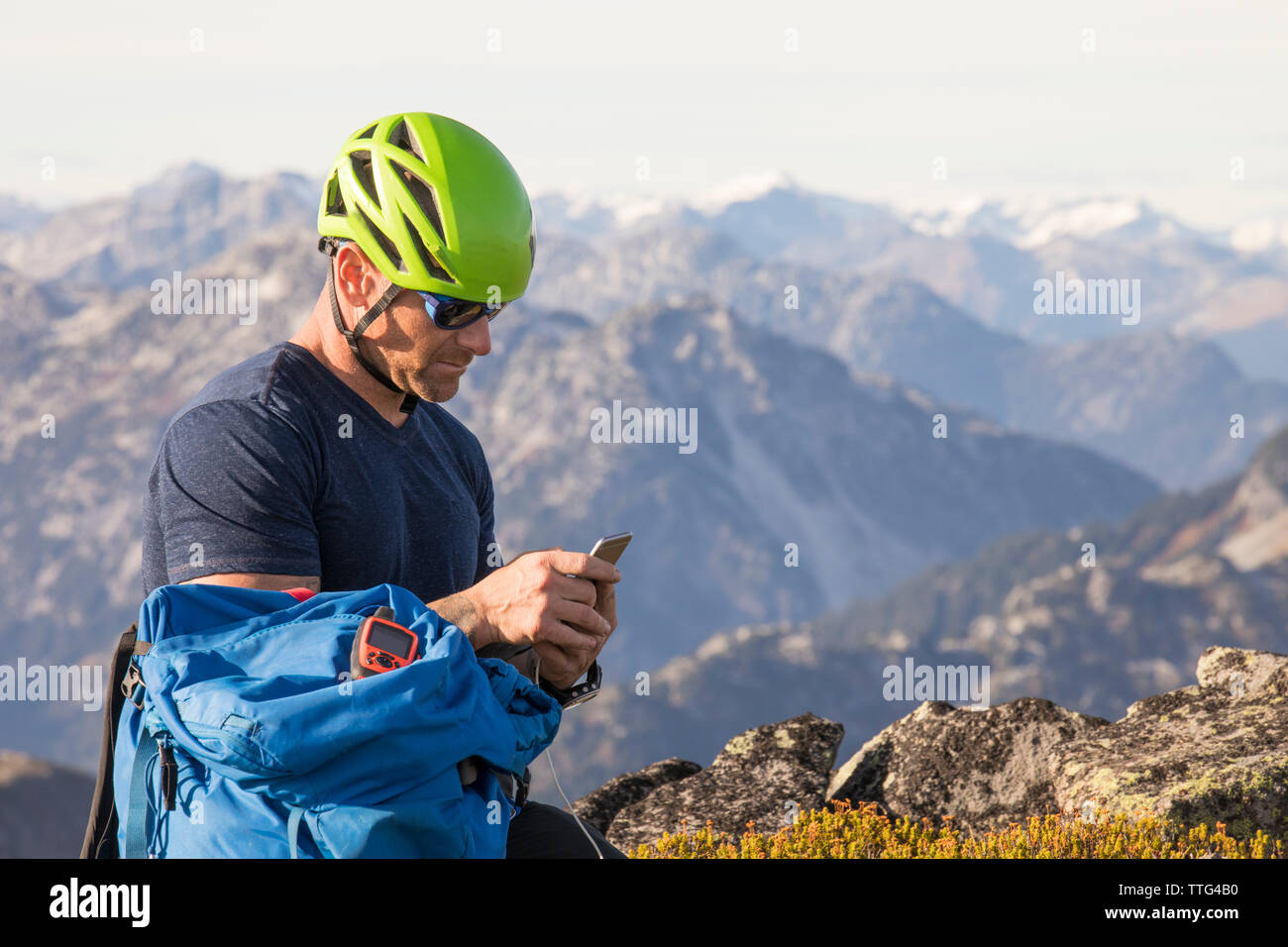 Un scalatore invia un messaggio di sicurezza utilizzando il suo smartphone dal vertice. Foto Stock