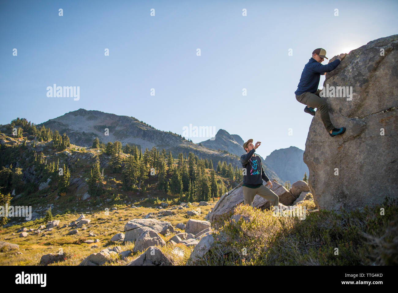 Scalatore bouldering sulla grande roccia con spotter qui di seguito. Foto Stock