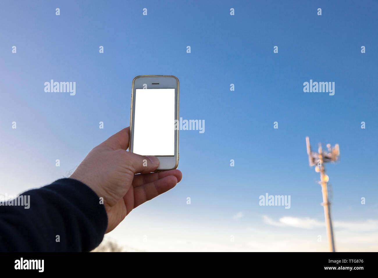 L'uomo detiene il telefono cellulare sul lato rivolto verso l'antenna di telefonia Foto Stock