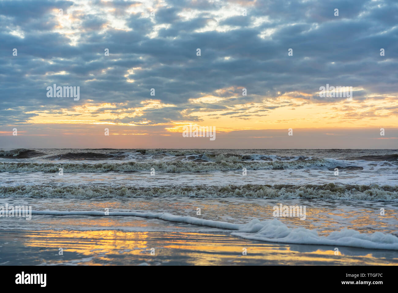 Oceano onde rush verso la spiaggia sabbiosa che riflette cielo incandescente di sunrise Foto Stock