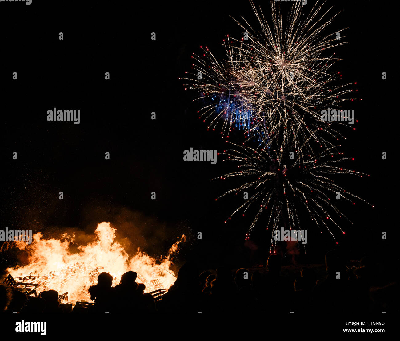 La gente vicino al grande fuoco tra le tenebre e fuochi d'artificio in cielo Foto Stock