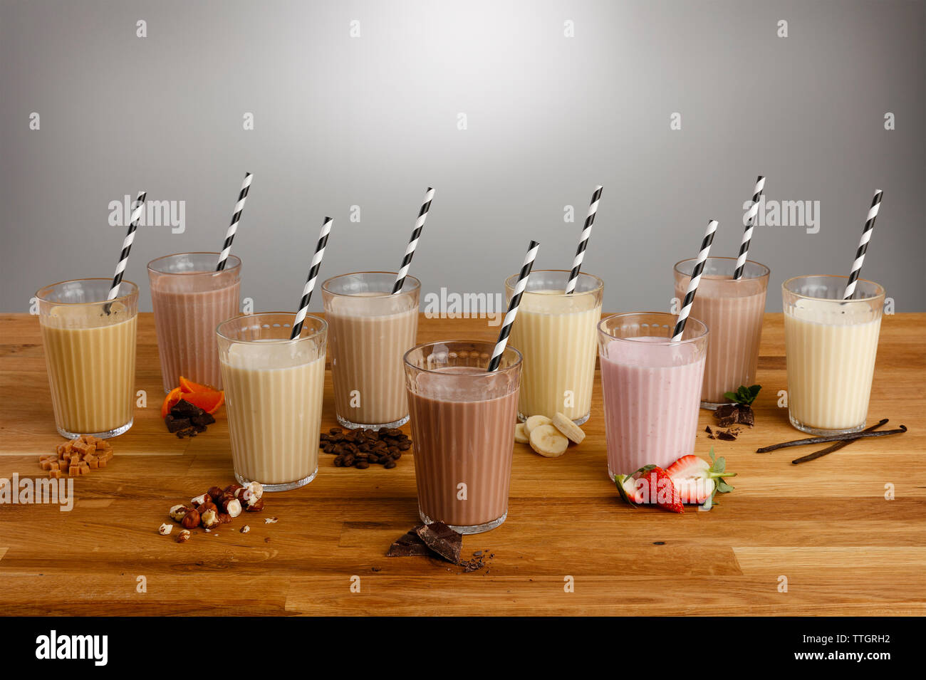Vetri di vari tipi di frullato colorato con cannucce di carta e gli ingredienti su un tavolo di legno top Foto Stock