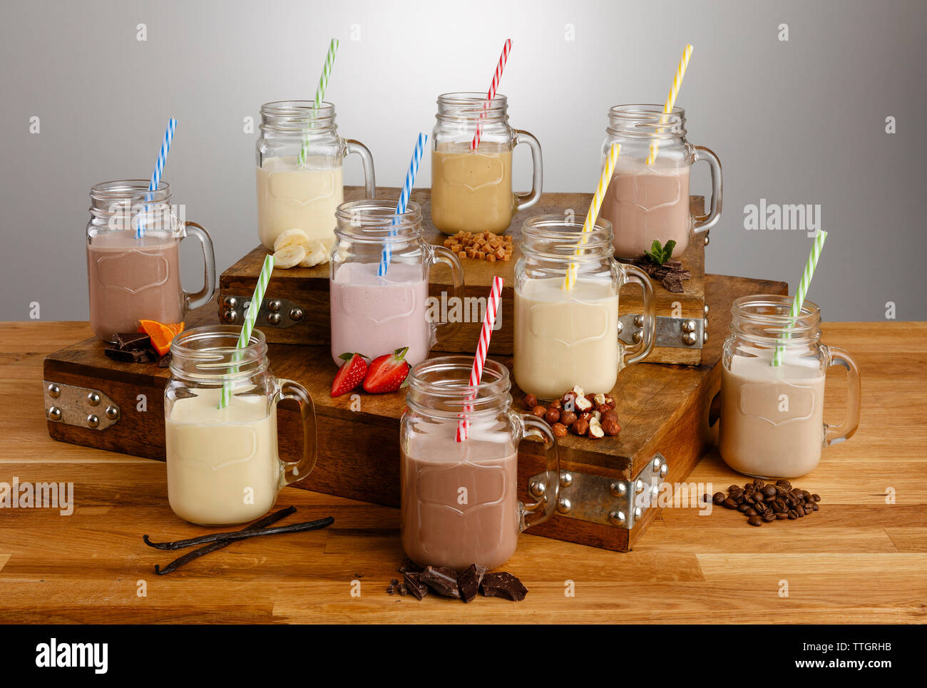 Vari tipi di frullato colouful e gli ingredienti nel vaso del muratore di occhiali con cannucce di carta su un tavolo di legno top Foto Stock