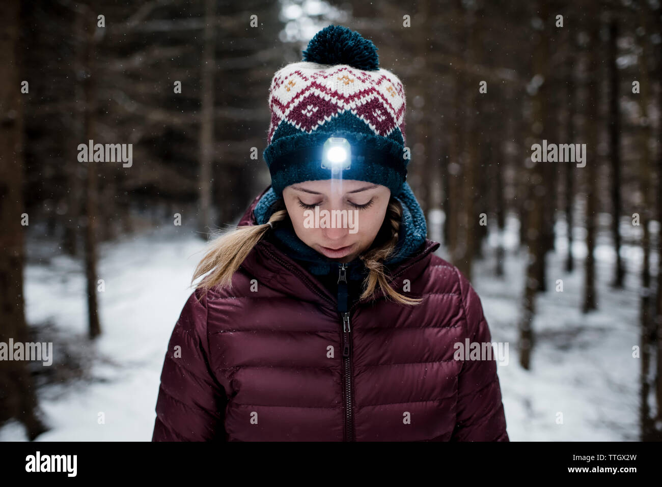 Donna che guarda in basso nella foresta con torcia da testa su mentre nevicava Foto Stock