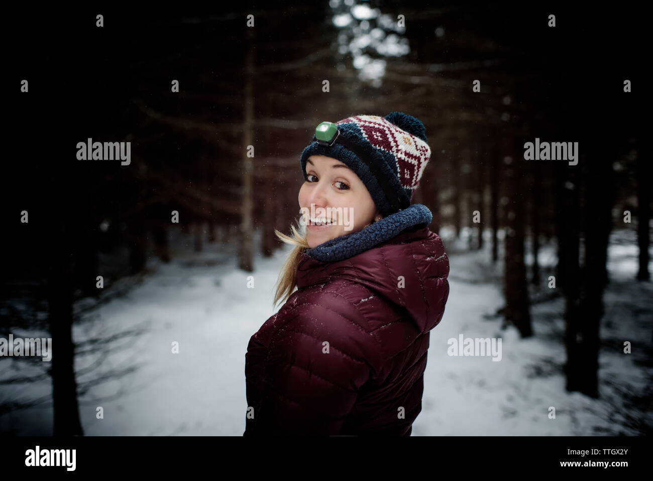Donna felice all aperto con la torcia da testa su nella foresta con la neve Foto Stock