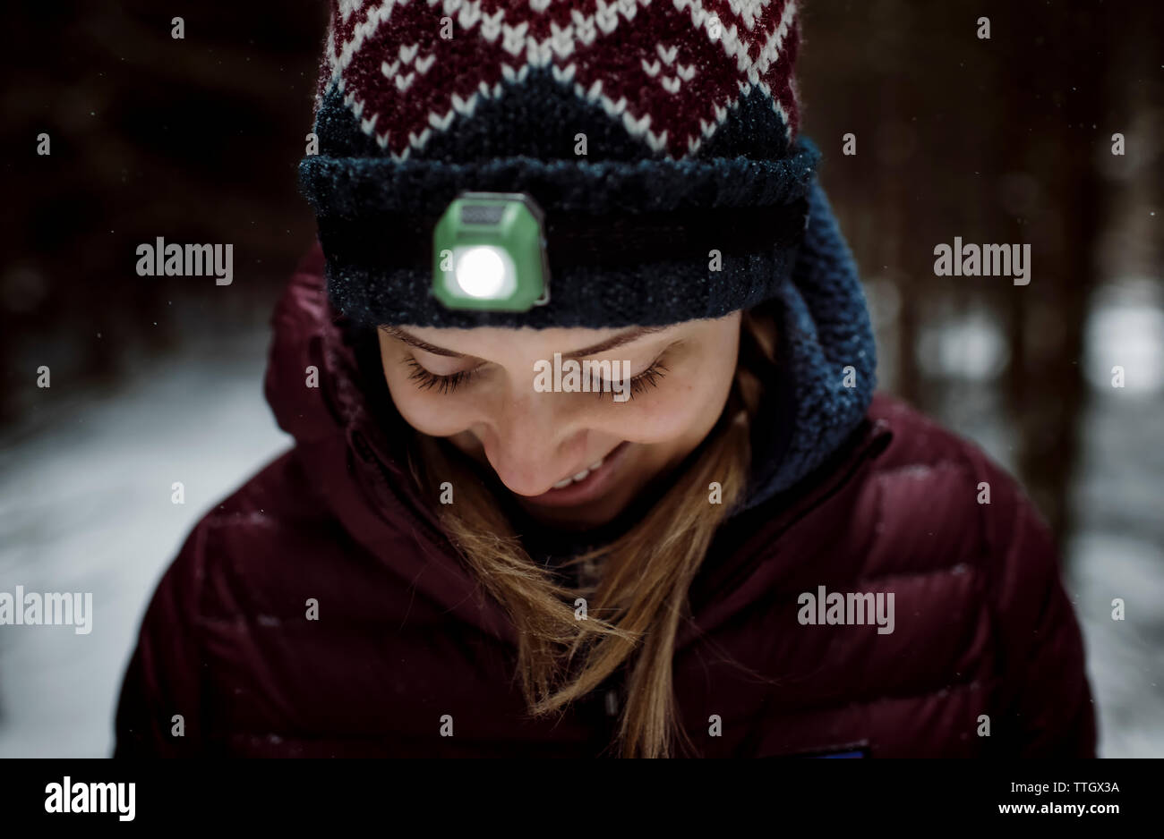 Donna bionda sorridente con la torcia da testa su all'aperto nella neve Foto Stock