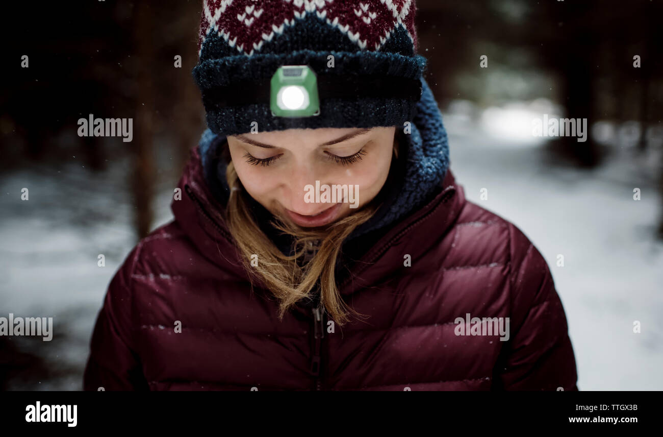 Donna bionda sorridente all'aperto nella neve con la torcia da testa su Foto Stock