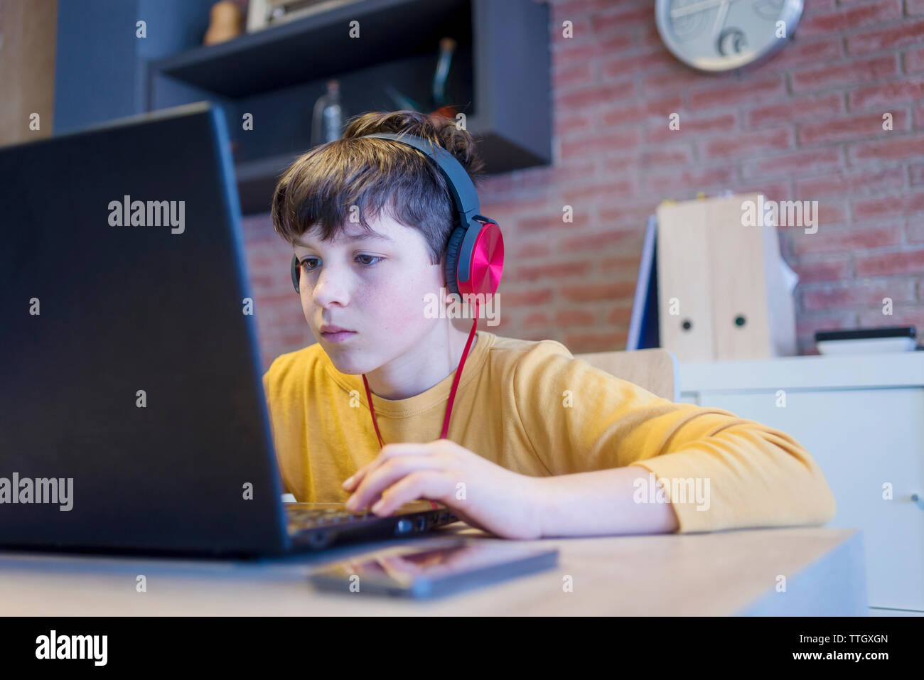Ragazzo focalizzato l'apprendimento utilizzando il computer portatile e le cuffie a casa Foto Stock